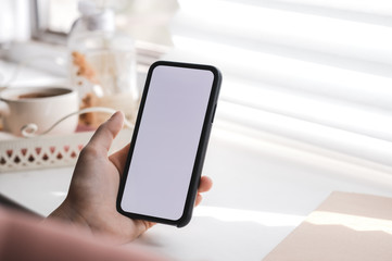 Woman uses a smartphone with a white screen, near the window at home in the morning. Mock up