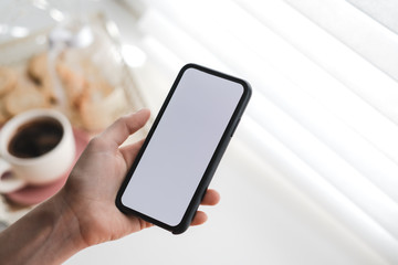 Woman uses a smartphone with a white screen, near the window at home in the morning. Mock up