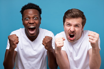 Happy two male friends in white t-shirt posing isolated on blue background. Sport leisure lifestyle concept.
