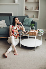 Beautiful caucasian female with short dark hair in a white cozy sweater sits in the living room and thinks about her future
