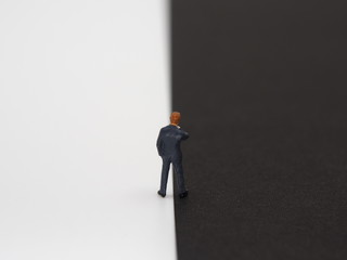 A miniature businessman standing on the white and black border.Good and evil concept image.
