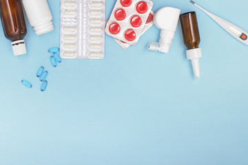 Various medicines, a thermometer, sprays from a stuffy nose and a pain in a throat on a blue background.