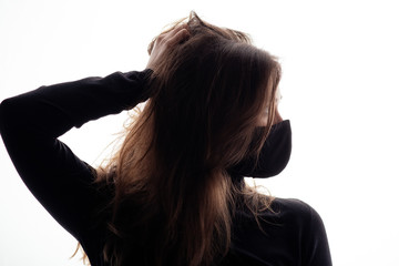 silhouette of young woman in black protective mask on a white background, girl posing like model with hand on disheveled hair,concept of quarantine fatigue and epidemic fashion