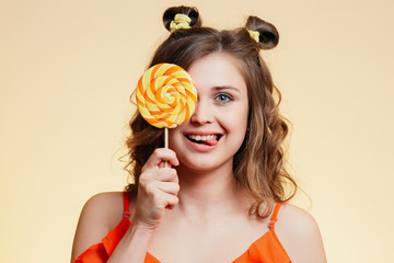 portrait of cute girl covering eye with round caramel on a colored background, happy woman with candy shows tongue , the concept of sweets, positive mood