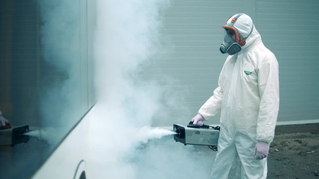 Sanitary worker is fumigating bus exterior
