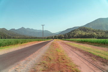 Beautiful mountain landscape with sugar cane fields foreground. Dramatic view of Road, fields, trees, green forest, farm, mountains, blue sky & road. Shot in Walsh's Pyramid, Cairns, Australia.