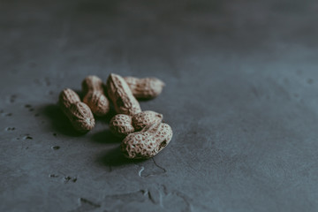 A close-up of a group of whole unpeeled dried peanuts in shell on a concrete blue textured background. A culinary and concept. Copy space. Soft focus. Natural background
