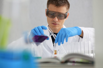 A male chemist holds test tube of glass in his hand overflows a liquid solution of potassium permanganate conducts an analysis reaction takes various versions of reagents using chemical manufacturing