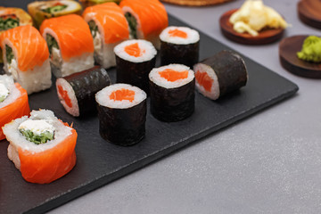 Set of sushi with wasabi, soy sauce and teapot on black stone background