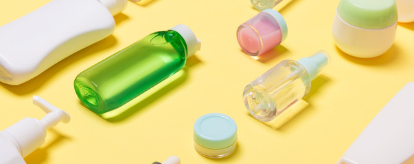 Composition of different sized cosmetic jars and bottles on yellow background. Beauty care concept with copy space