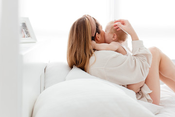 A beautiful young mother calms, kisses, hugs and puts her baby baby to sleep in the bright bedroom of the house