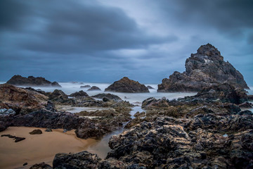 Fototapeta na wymiar Long Exposure of rocks at the beach of the Camel Rock bay in New South Wales, Australia at a cloudy and windy day in summer with strong waves in the ocean. 