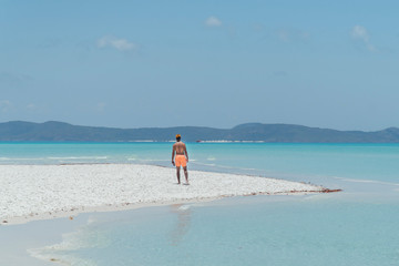 Man on paradise blue beach. Tourist on Whitsundays beach, white sand, in orange shorts, hat with aqua turquoise ocean. Travel, beauty, holiday, vacation, exotic. Whitsundays Islands, Australia.