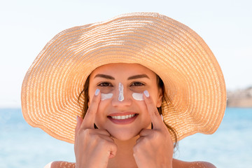 Smiling woman in hat is applying sunscreen on her face. Indian style