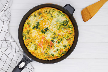 Homemade frittata or omelette with mix of vegetables in iron skillet on white table,
