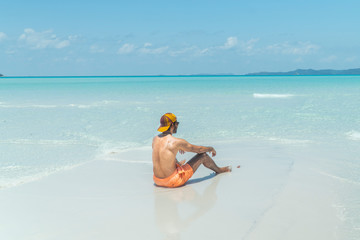 Man on paradise blue beach. Tourist on Whitsundays beach, white sand, in orange shorts, hat with aqua turquoise ocean. Travel, beauty, holiday, vacation, exotic. Whitsundays Islands, Australia.