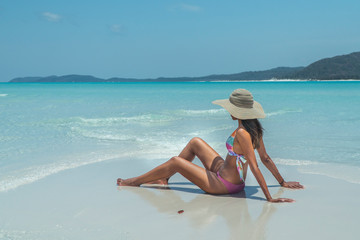 Fototapeta na wymiar Woman sitting on paradise beach. Tourist on Whitsundays beach, white sand, in pink bikini & hat, with aqua blue turquoise ocean. Travel, holiday, vacation, exotic. Whitsundays Islands, Australia.