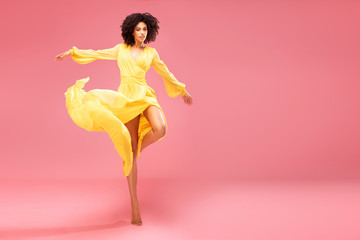 Afro girl dancing in yellow maxi dress.