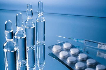 Glass ampoules with syringe and pills on a blue background. Preparing a doctor for an injection of...
