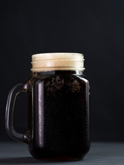 A glass Can of dark beer with a handle on a concrete table