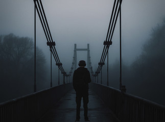 The silhouette of a lone man on a dark, foggy morning on the old bridge over the river. foggy...