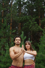 Fototapeta premium Healthy lifestyle, sport, yoga and people concept - beautiful couple doing yoga together over green woods background