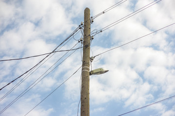 Electric wooden pole with lamp and electricity cables hanging on