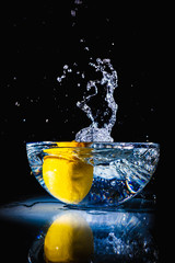 Water splash from a lemon falling into a bowl with water on black background and reflection