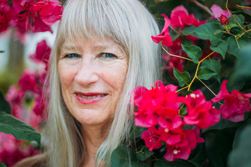 Happy healthy beautiful senior woman at her 70-80 beauty portrait in tropical summer smiling from the flower bush