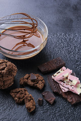 Desserts. Chocolate and cookies. Melted chocolate with a whisk in a transparent bowl. Dark cookies, dark and light pink white chocolate on a black background. Background image, copy space