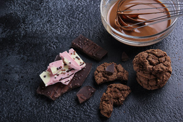 Desserts. Chocolate and cookies. Melted chocolate with a whisk in a transparent bowl. Dark cookies, dark and light pink white chocolate on a black background. Background image, copy space