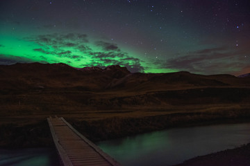 The northern lights light up the sky over a bridged river.