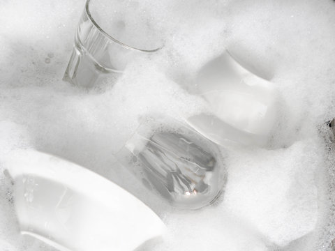 Various earthenware and glassware in soapy foam in sink with soapy water