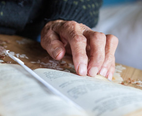 Old woman hand on the open prayer book.