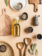 Flat lay of small bowls various dry spices, wood kitchen utensils, olive oil in glass bottle on beige background. Top view.