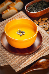 Roasted pumpkin and carrot soup with cream and pumpkin seeds on a wooden table.