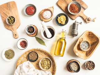 Various dry spices and sauces on light background. Flat lay of small bowls with dijon mustard, olive oil, ketchup, capers and spices. Top view