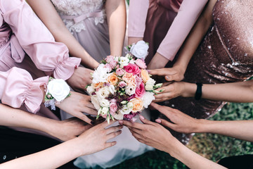Obraz na płótnie Canvas Wedding bouquet in the hands of the bride and bridesmaids with white pink yellow roses and greenery on a beige background