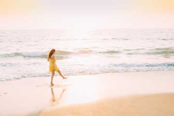 Fototapeta na wymiar Goa, India. Young Caucasian Woman In Yellow Dress Walking Along Seashore In Summer Sunlight