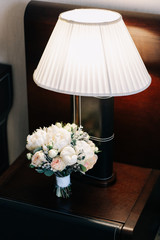 wedding bouquet with white peonies with yellow roses and a white ribbon near a cozy lamp in a classic style