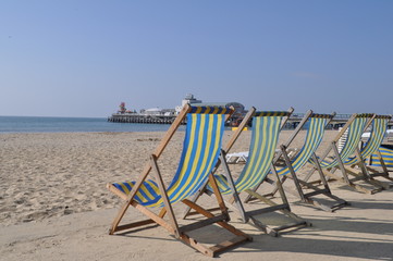 A row of blue and yellow striped deck chairs positioned on the Promenade in front of a sandy beach.