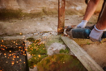 A young caucasian man with a grinder in his hand works in the yard