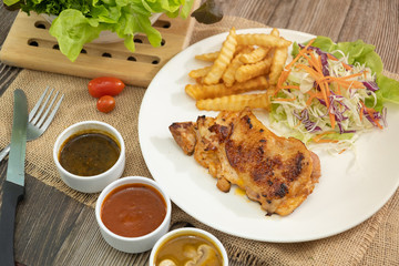 Plate of grilled chicken with french fries and vegetables bbq sauce, mushroom sauce and black pepper sauce on wooden table. 