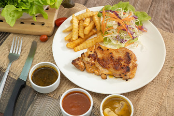Plate of grilled chicken with french fries and vegetables bbq sauce, mushroom sauce and black pepper sauce on wooden table. 