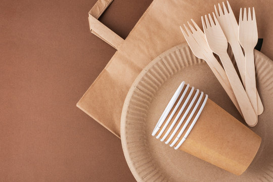 Eco-friendly Tableware On A Brown Background, Paper Plates And Glasses, Wooden Forks And Nomes, Top View