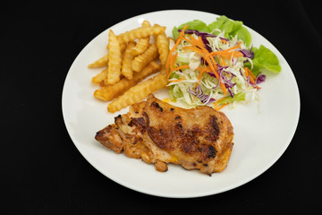 Plate of grilled chicken with french fries and vegetables on dark background- Stock photo