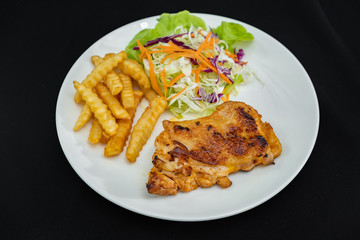 Plate of grilled chicken with french fries and vegetables on dark background- Stock photo