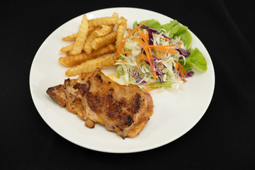 Plate of grilled chicken with french fries and vegetables on dark background- Stock photo