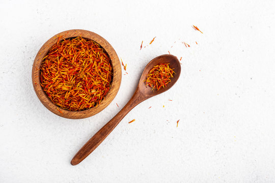 saffron in a wooden cup next to a wooden spoon on a white table top view