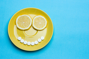 Vitamins, lemon and pills on a yellow plate